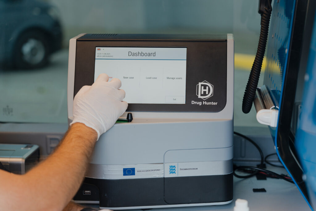 Close‑up of the Drug Hunter dashboard screen with a gloved hand navigating the menu.